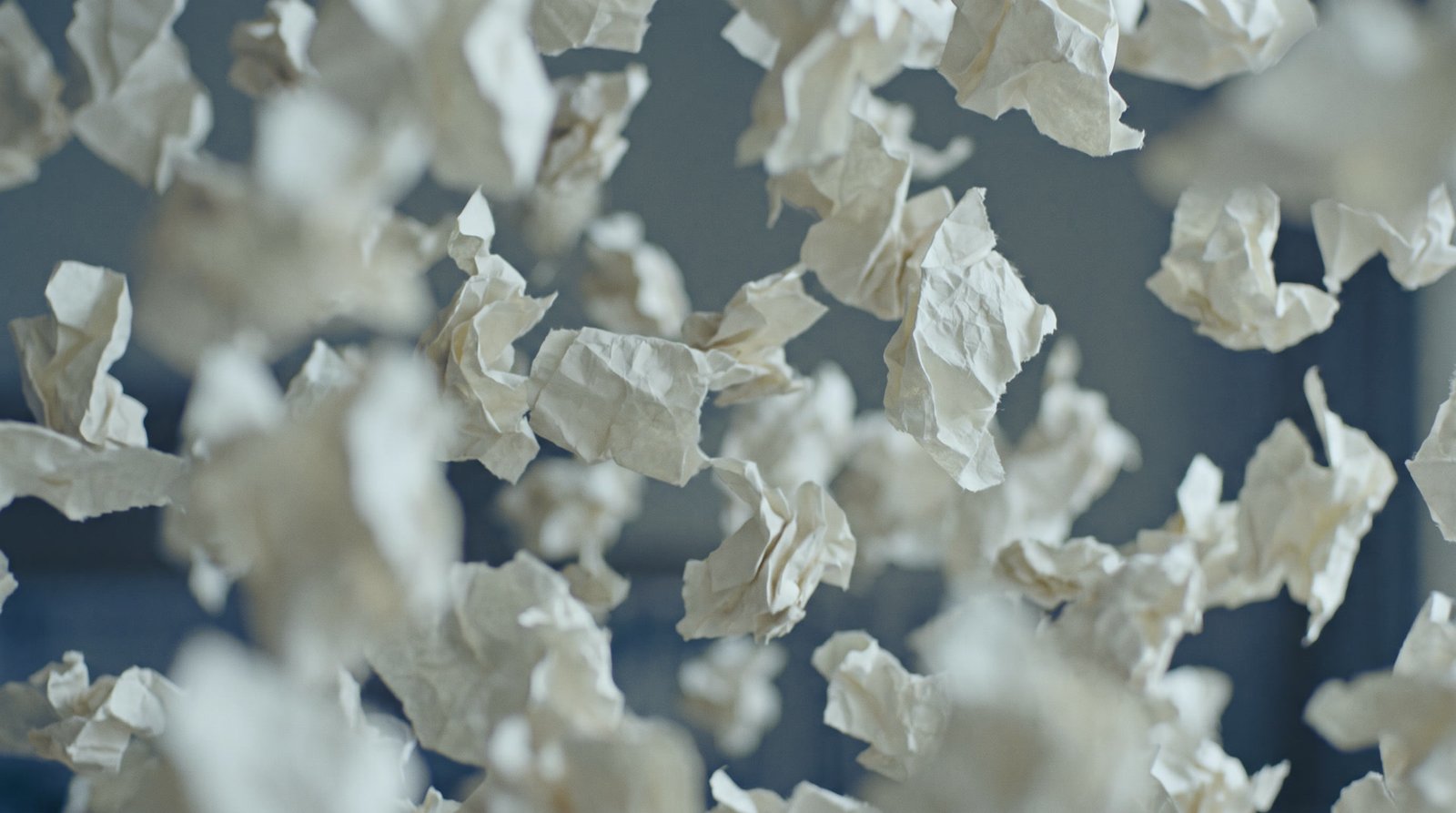 Paper scraps drifting in blue-grey fog, everything airborne at once